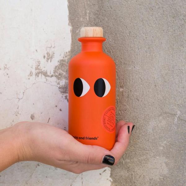Hand holding the 200ml vibrant orange bottle of chilli-infused extra virgin olive oil against a rustic wall.