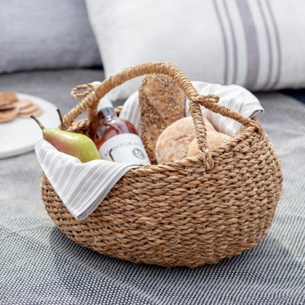 Natural seagrass picnic basket filled with fresh bread, wine, and fruit on a picnic rug.