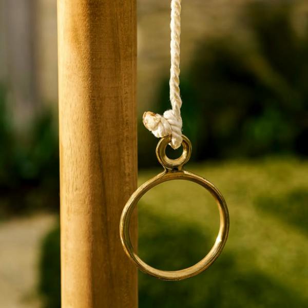 A close-up macro shot of a solid brass ring tied with a white rope knot hanging next to a smooth teak wood parasol pole.