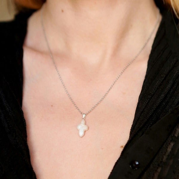 Model wearing white pearl cross pendant on delicate silver chain.
