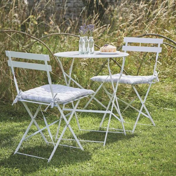 Chalk white metal folding bistro table and two chairs styled on a green lawn with lavender in bottles.