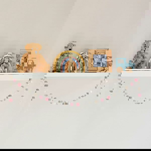 A Handmade Multicoloured Felt Ball Garland adorned handmade shelf showcasing three adorable teddy bears.