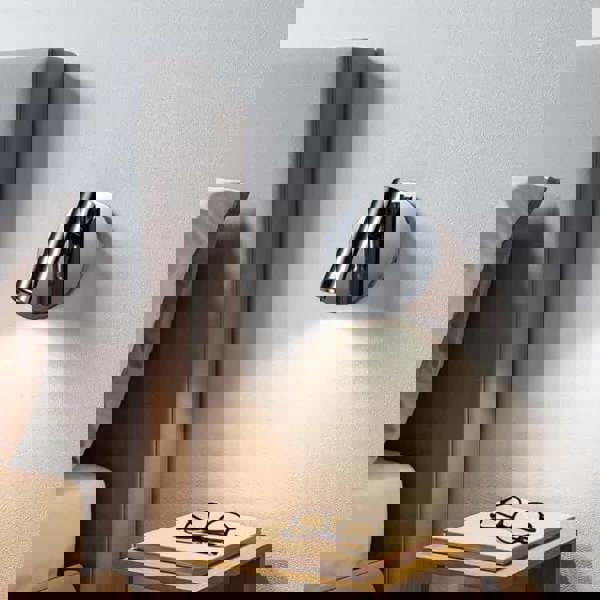 polished chrome bed reading lamp mounted on the wall next to a bed in a minimailst bedroom