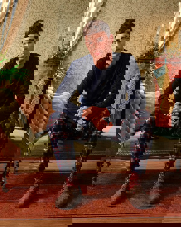 Man sitting on a couch wearing navy pajama top and plaid pants in a cozy living room.