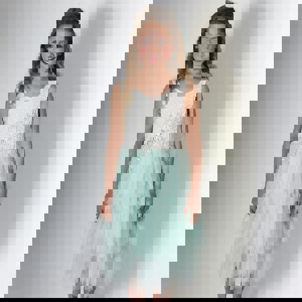 Young girl wearing a white lace top and light blue tulle skirt on a plain background