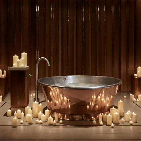 A cluster of ivory LED candles of various sizes surrounding a copper bathtub.