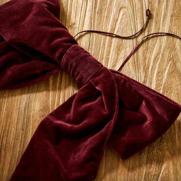 A plush berry red cotton velvet Christmas door bow with a thin matching hanging loop, laying flat on a rustic wooden table.