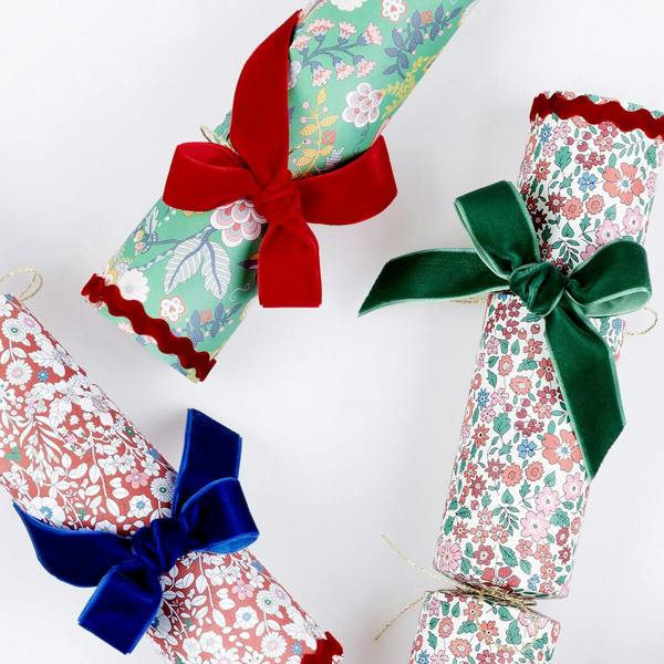 Close-up detail of Liberty print Christmas crackers showing red ric rac scalloped edges and plush red, dark green, and royal blue velvet bows.