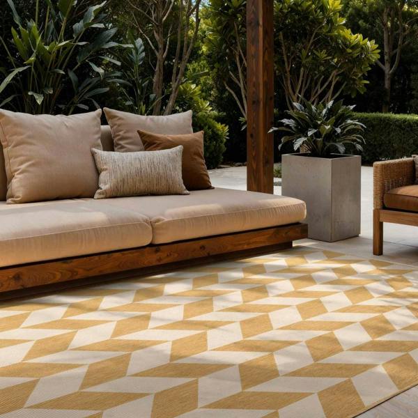 Outdoor seating area with a beige sofa, patterned rug, and potted plants.
