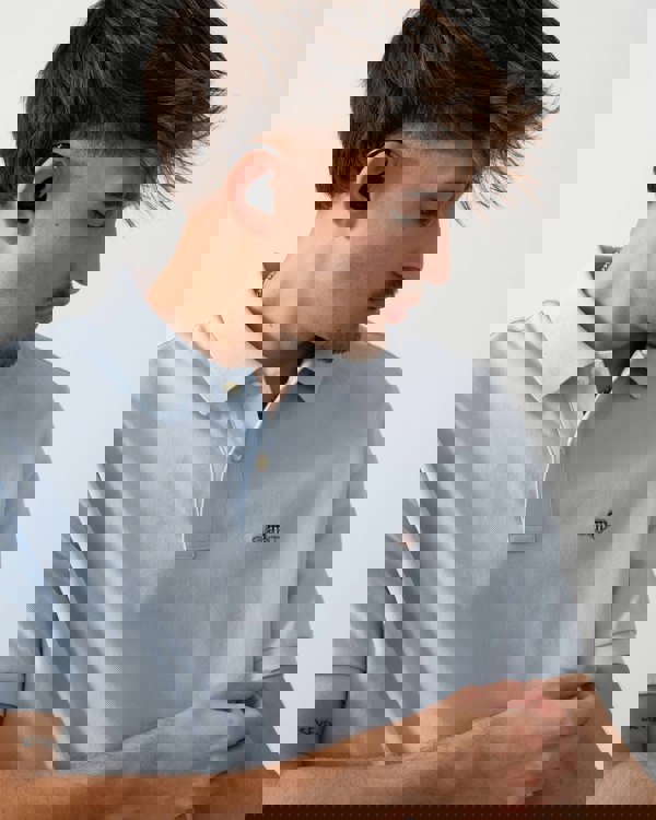 detail shot of a model wearing a GANT Mens Regular Fit Short Sleeve Shield Logo Pique Polo in Fresh Blue