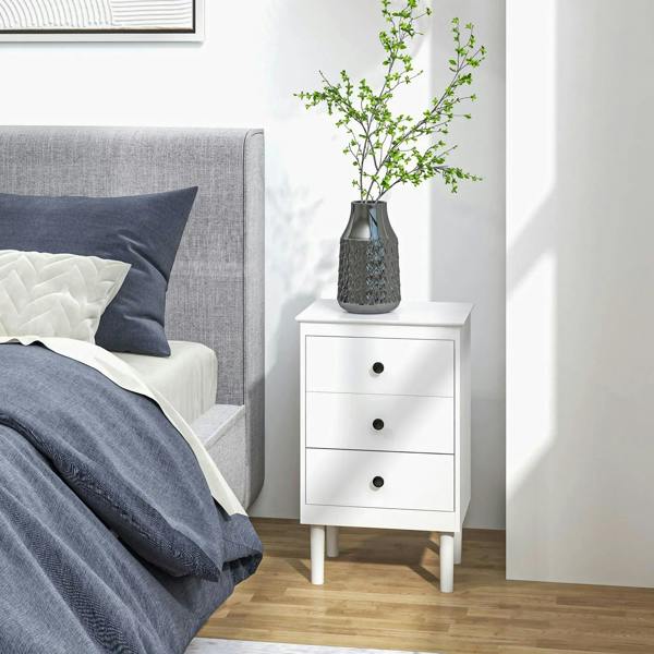 White three-drawer bedside table with round black knobs, vase and branch decor.