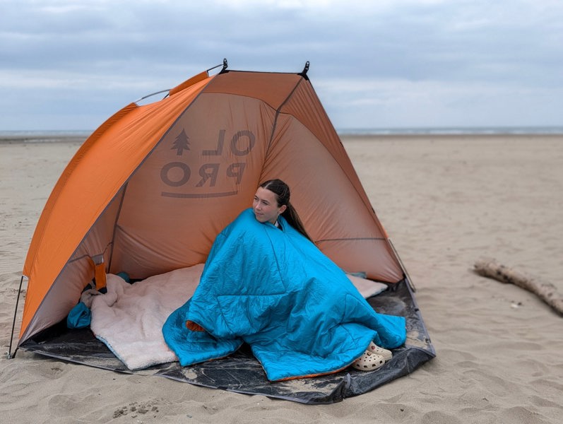 Someone using the OLPRO Insulated Outdoor Reversible Blanko on the beach whilst sat inside of a beach tent.