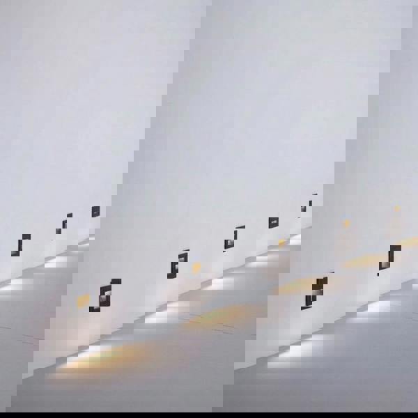 black stair step lighting mounted in a row on a white wall at low level 