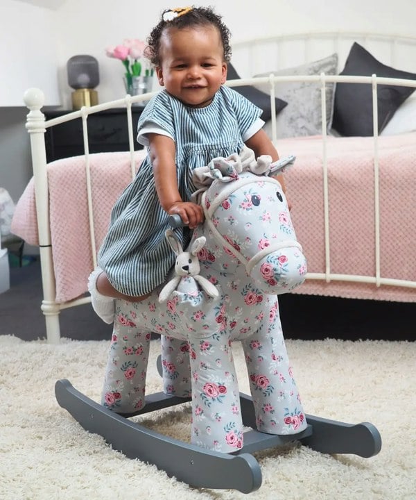 little girl playing on floral rocking horse in nursery room 