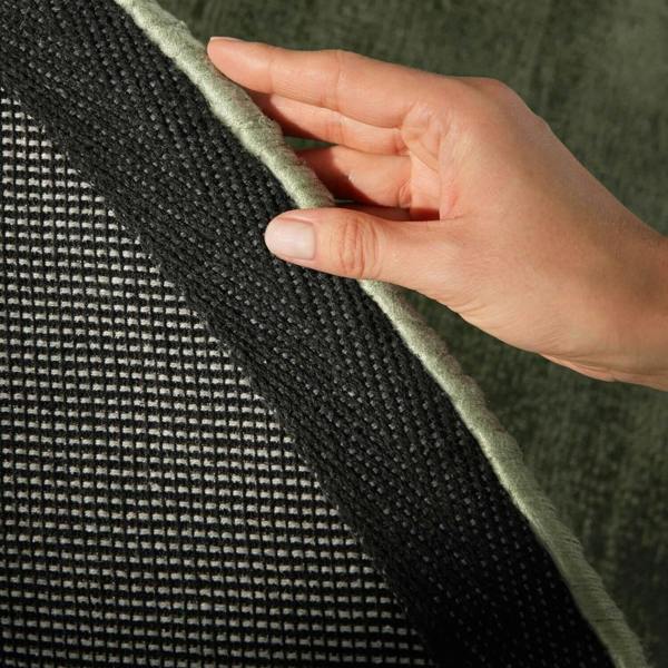 Hand touching the edge of a green fabric with a black woven pattern