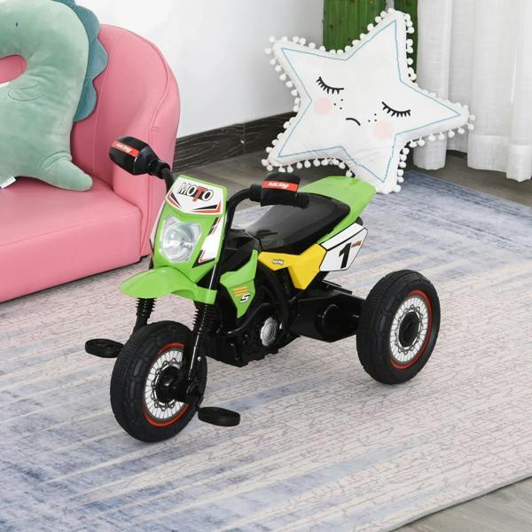 Green and yellow kids ride-on motorcycle trike with handlebar grips and front headlight on indoor floor.
