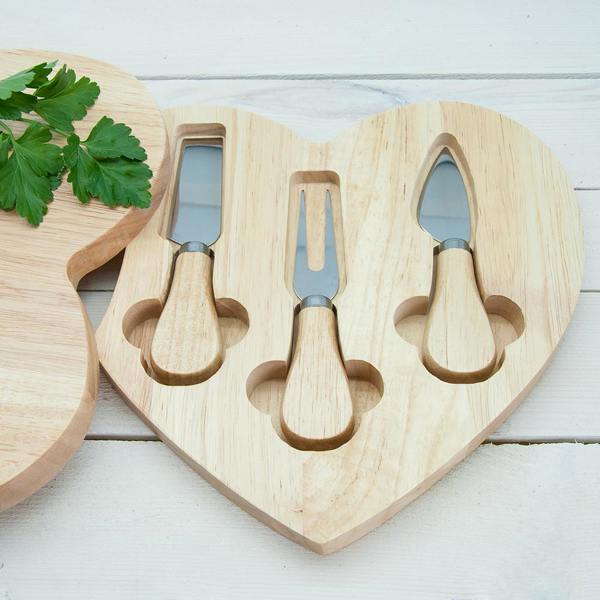 A heart-shaped wooden cheese board swung open to reveal a hidden storage compartment containing three stainless steel cheese knives with matching wooden handles.