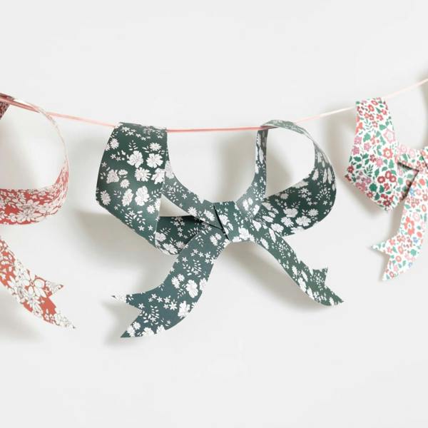 Close-up of 3D paper bow pennants featuring intricate green and red Liberty floral prints strung on a pink velvet ribbon.