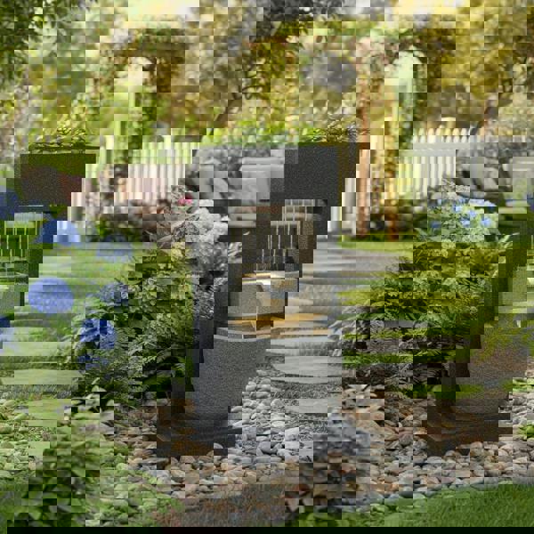 Sleek black electric water feature with cascading water, surrounded by vibrant flowers and lush greenery in a serene garden setting