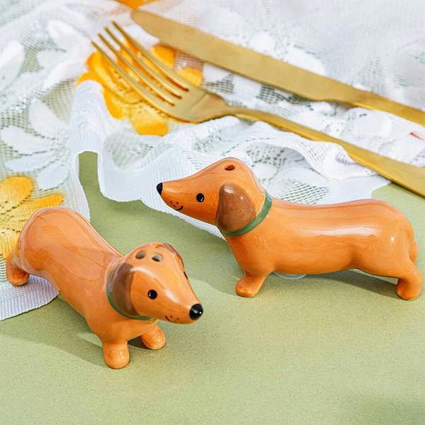 Two ceramic brown dachshund salt and pepper shakers arranged on a green tabletop next to a gold fork and knife.