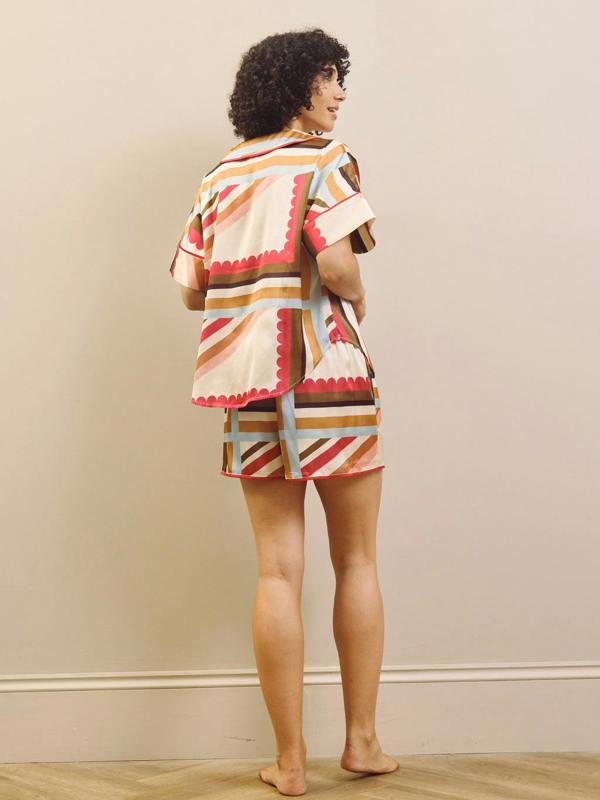 Woman wearing a colourful patterned short pyjama set against a beige background