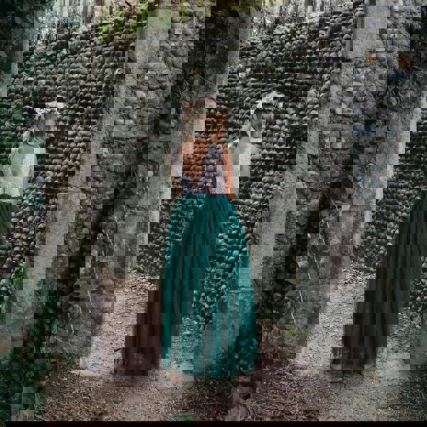 Girl in a white top and teal skirt standing in front of a stone wall.