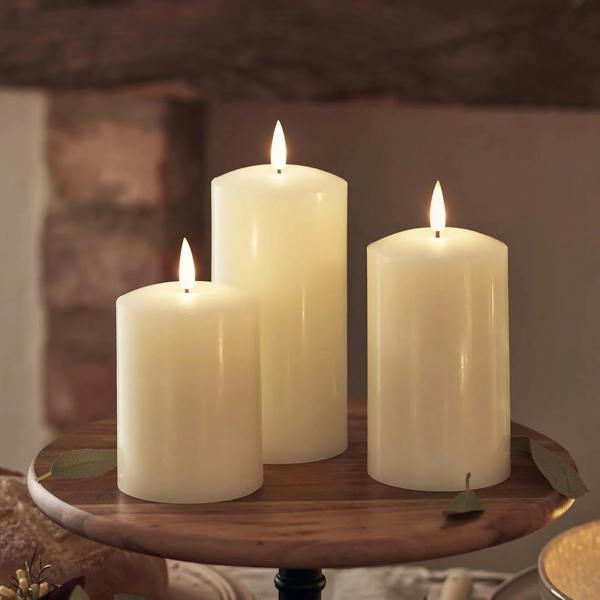Staggered trio of TruGlow ivory rechargeable LED pillar candles with flickering flames on a white background.