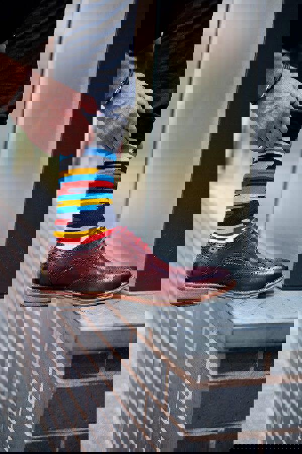 Person wearing a colorful striped premium sock with a brown shoe on a brick wall background