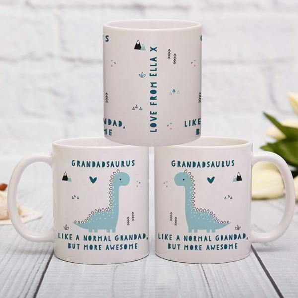 A personalised white ceramic mug displaying a green dinosaur illustration and custom name text, styled on a wooden tabletop.