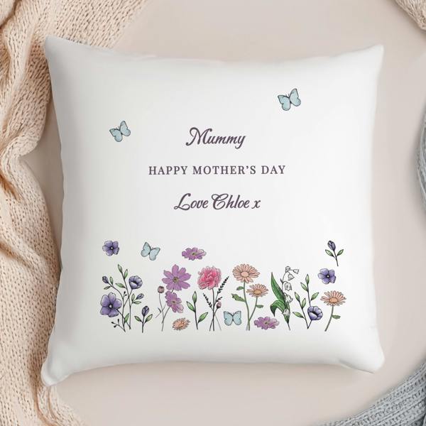 A personalised white cushion printed with a wildflower border and the text 'Mummy Happy Mother's Day Love Chloe x' framed by soft knitted blankets.