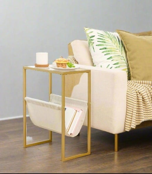 Slim gold side table with clear glass top and linen fabric magazine rack, perfect for small spaces like bedrooms or narrow living room corners

