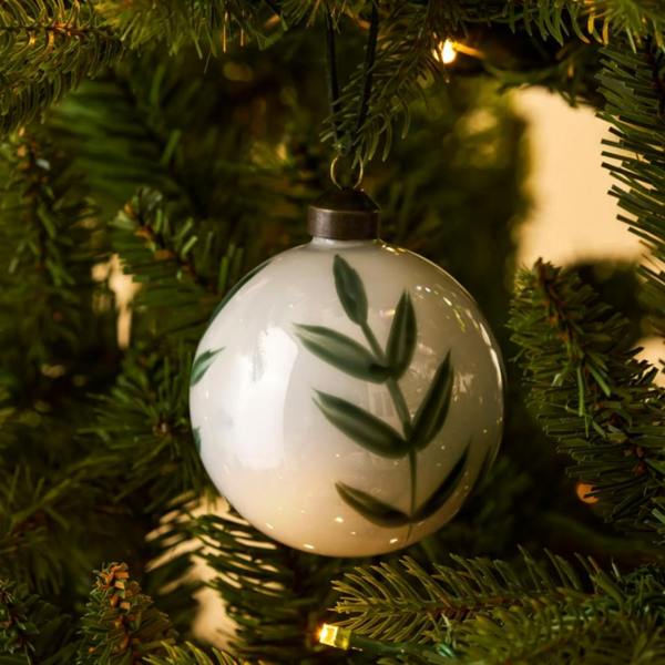 A single Bibury hand-painted glass rosemary Christmas bauble with a pearl finish hanging from a green pine branch.