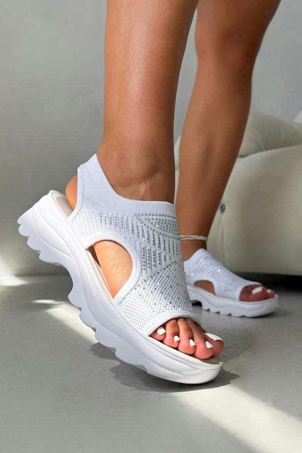 White sandals with a thick sole worn by a person on a neutral background