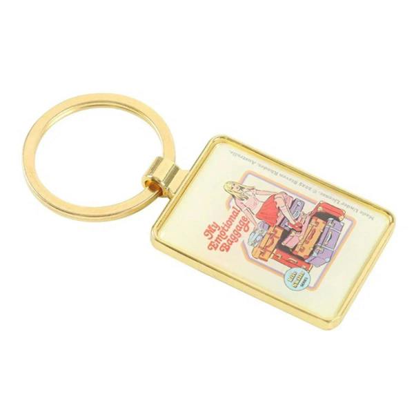 Gold keychain charm angled view, with illustrated suitcase scene.