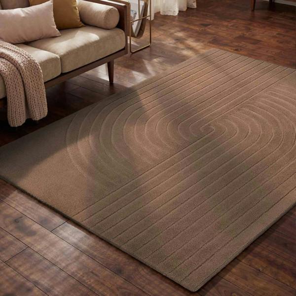 Brown textured rug on a wooden floor with a beige sofa in the background