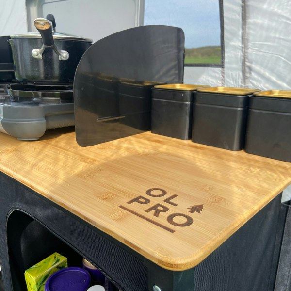 The OLPRO Deluxe Camp Kitchen With Double Cupboard pictured with a stove on top of it with pans on the stove.