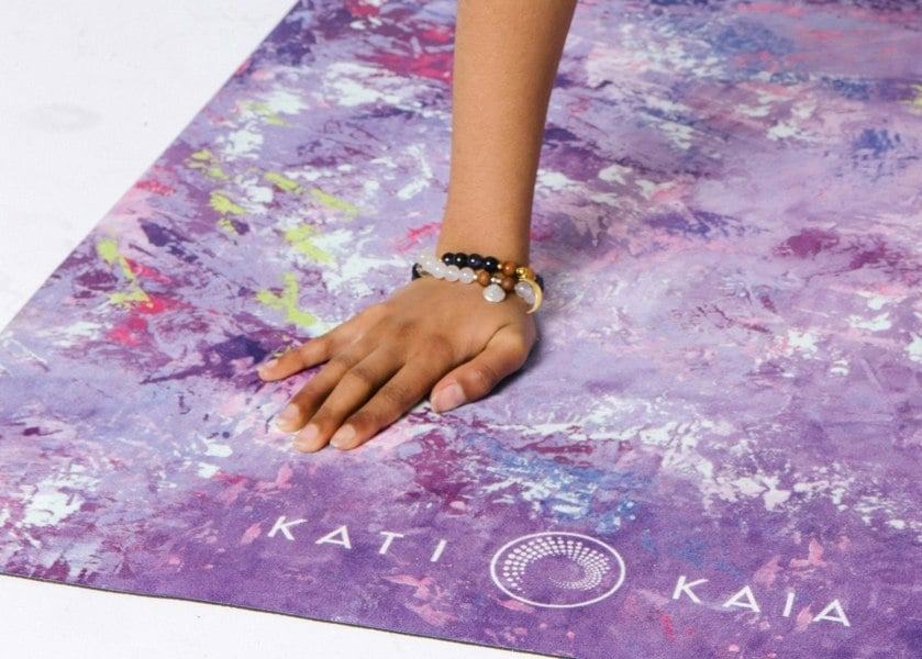 Hand wearing moonstone mala necklace set on purple Kati Kaia yoga mat with artistic design