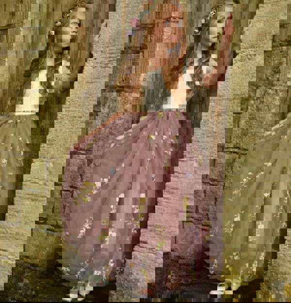 Young girl in a floral dress standing against a stone wall