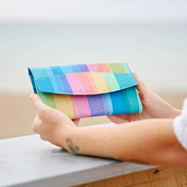 A woman is holding a Recycled Plastic Rainbow Pouch by the beach.