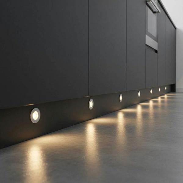 Chrome LED plinth lights mounted at low level in a dark grey kitchen plinth. 