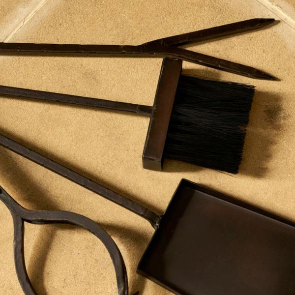 An overhead view of individual fireplace tools—the poker, brush, ash shovel, and log grabber—laid out on a stone flagstone hearth.