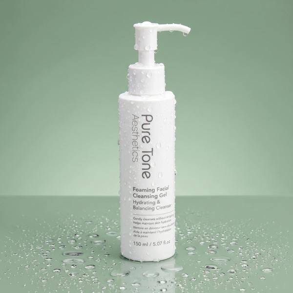 Pure Tone Aesthetics Foaming Facial Cleansing Gel standing on a reflective green surface with water droplets on the bottle and surrounding surface