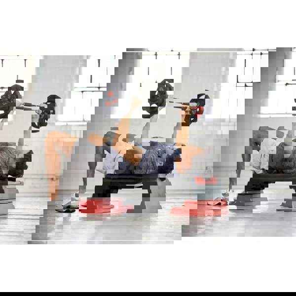 Man lifting a barbell lying on a Reebok Step platform- Red