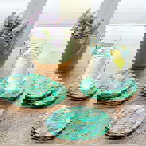 Four recycled coasters made from plastic on a table next to a glass of water.