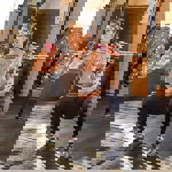 Woman performing a squat with a barbell in a gym setting wearing  adidas wrist wraps