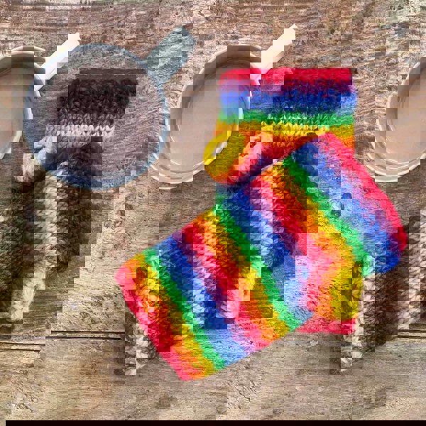 A pair of Woollen Rainbow Handwarmer Gloves next to a cup of coffee.