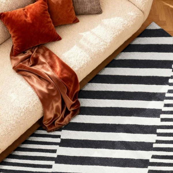 Beige sofa with orange cushions and a brown blanket on a black and white striped rug.
