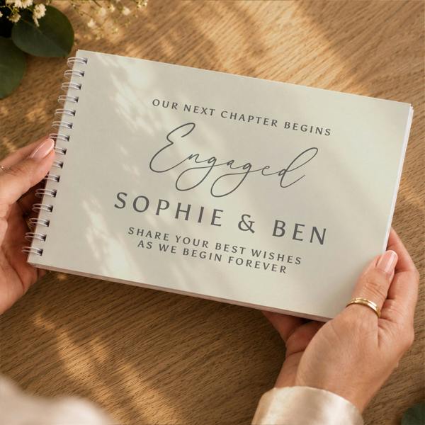 Hands holding the Personalised Engagement Guest Book reading Our Next Chapter Begins Engaged Sophie and Ben by Abode Home & Gifts