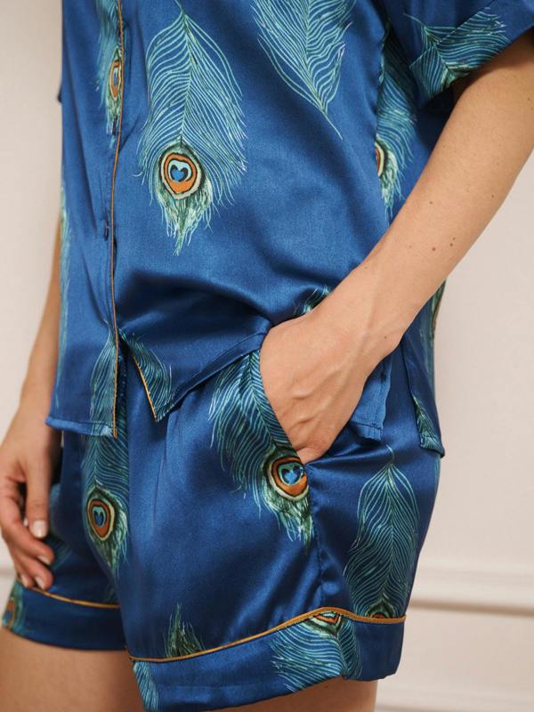 Model wearing a blue satin short pyjama set with peacock feather pattern against a white background. pocket detail