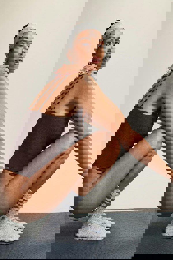 Brown textured bamboo cross-back bodysuit in soft brown fabric, designed for activewear and athleisure. Featuring breathable, moisture-wicking bamboo material that offers stretch and comfort for yoga, Pilates, or everyday layering. The cross-back detailing adds a stylish touch, making it perfect for transitioning from workouts to casual wear.